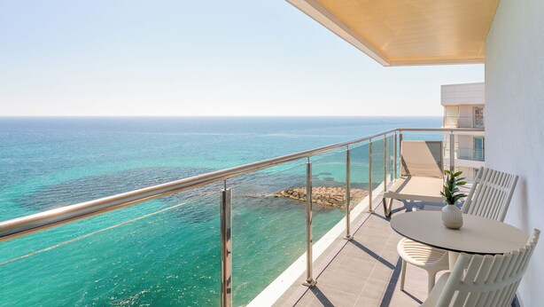 A balcony with a view of the ocean, a round table with a vase, and a chair. - Melia Alicante (Alicante)