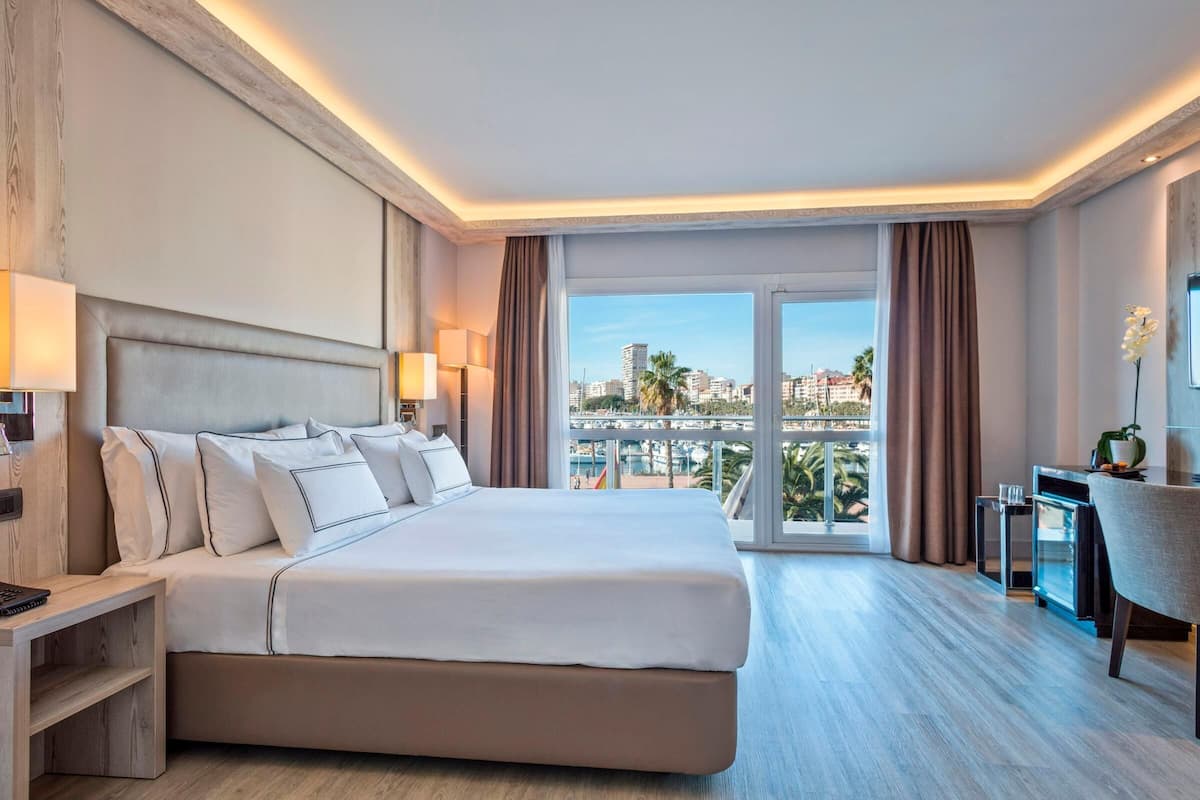 A hotel room with a large bed, a desk, a chair, and a view of the city.