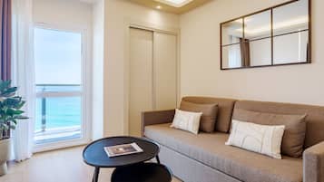 A modern living room with a sofa, a small table, a potted plant, and a view of the sea through a large window.