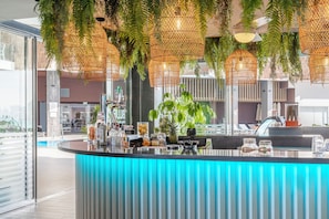 A modern bar area with hanging wicker lamps, a counter with various items, and a view of the pool outside. - Melia Alicante (Alicante)