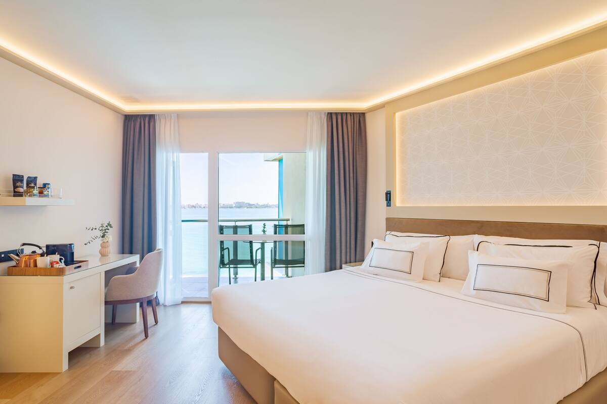 A modern hotel room with a large bed, a desk, and a balcony with a view.
