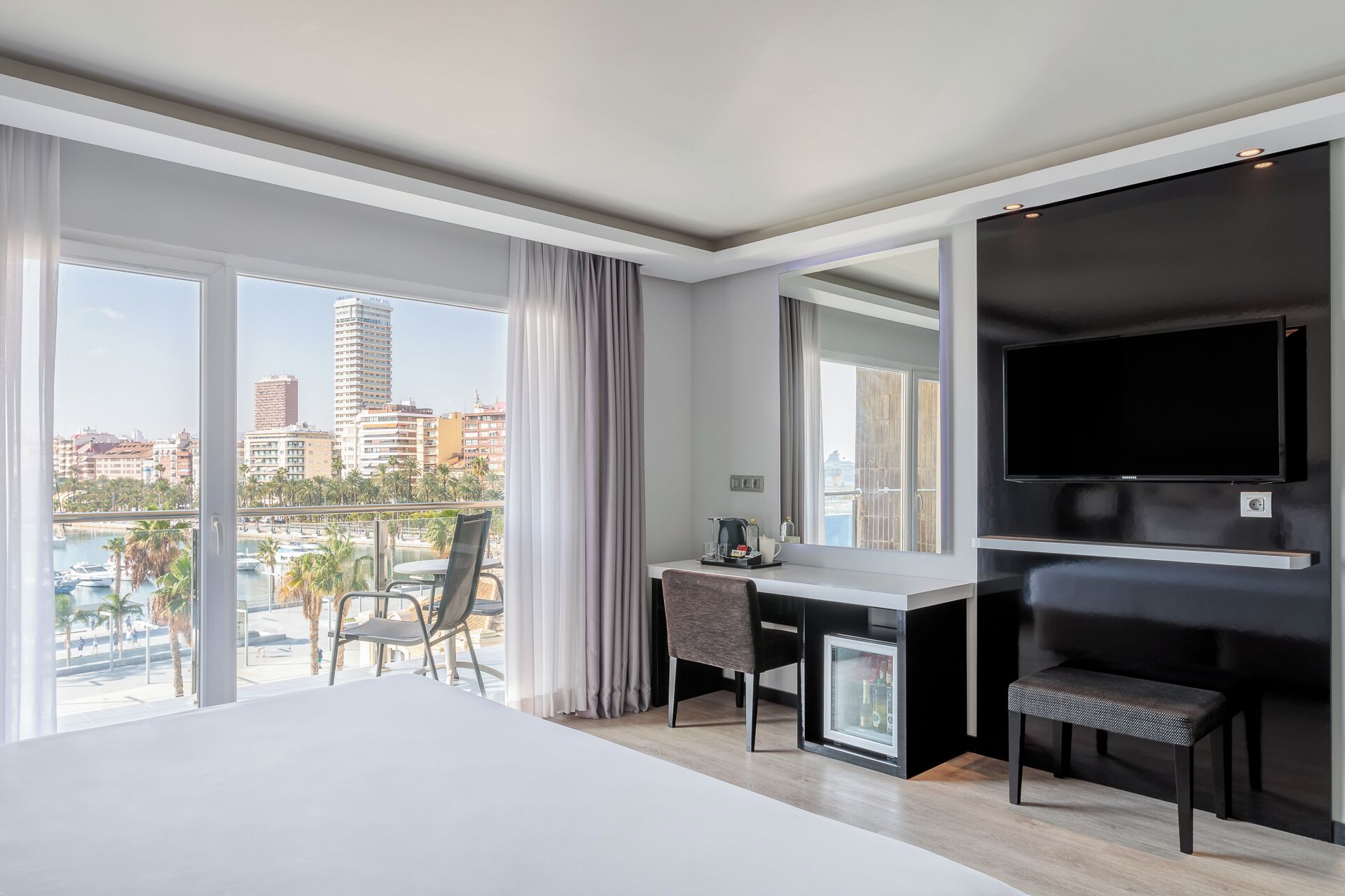 Une chambre d’hôtel moderne dotée d’un grand lit, d’un bureau, d’une chaise, d’une télévision et d’un balcon offrant une vue sur la ville.