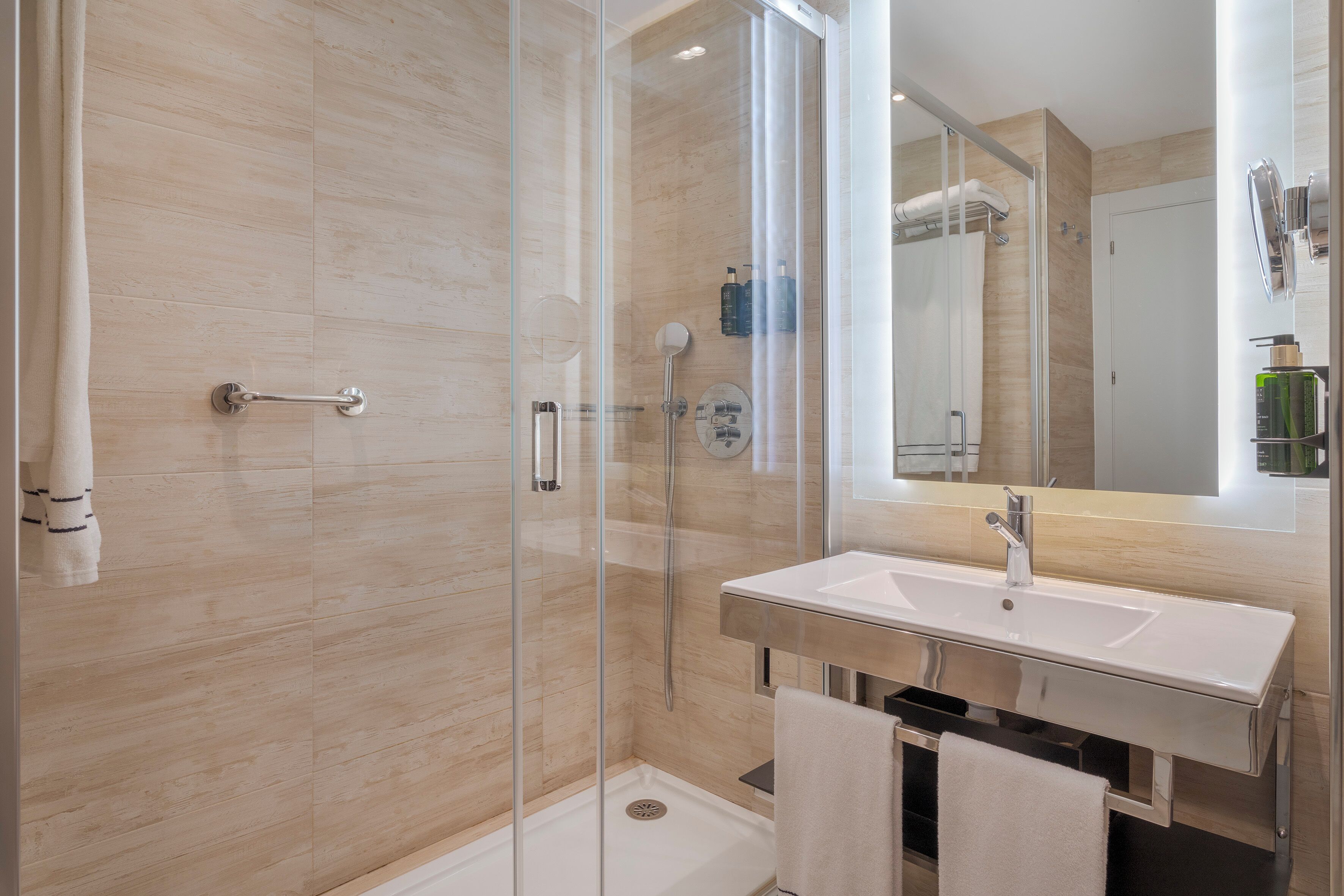 Un baño moderno con ducha de vidrio, lavamanos blanco y un espejo grande.