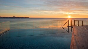 A clear view of a swimming pool with a glass barrier, a wooden deck, and a sunset over the water. - Melia Alicante (Alicante)