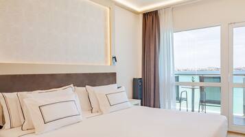 Habitación de hotel con una cama grande, vistas a la ciudad a través de la ventana y un balcón con mesa y sillas.