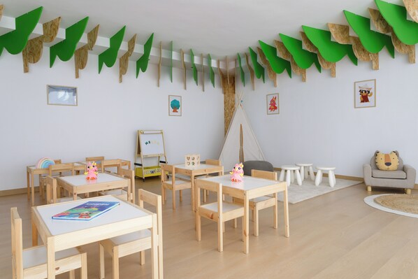 A children's playroom with wooden tables and chairs, a whiteboard, and a tent. - Melia Alicante (Alicante)