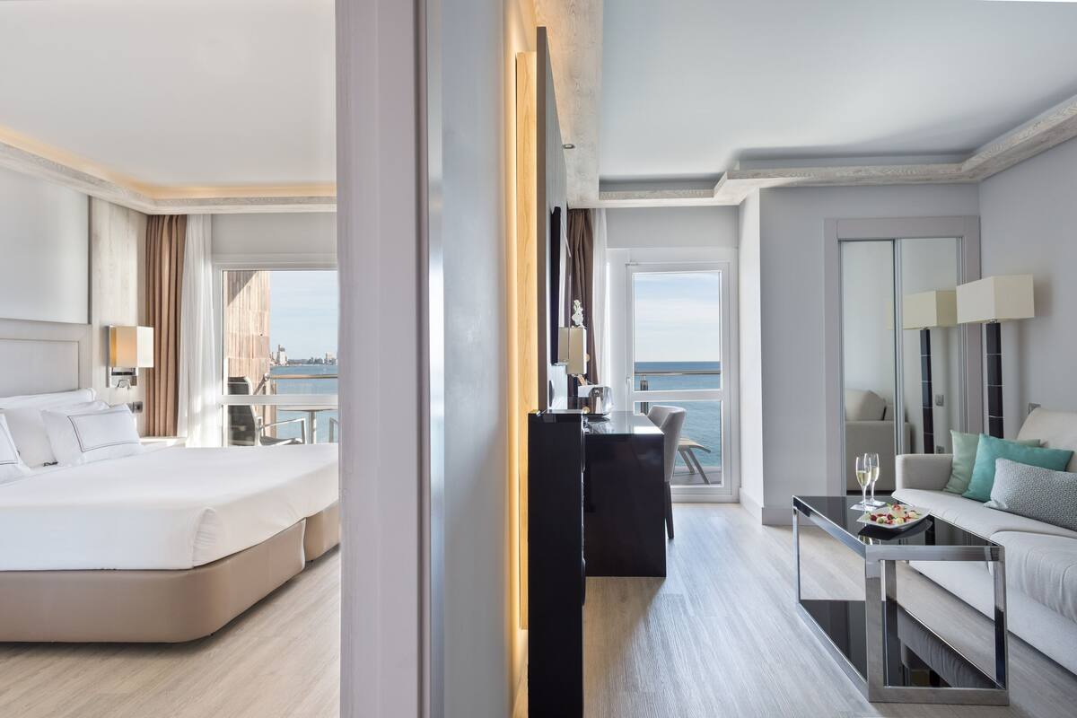 A modern hotel room with a bed, a desk, a sofa, and a view of the city.