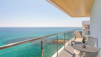 A balcony with a view of the ocean, a table with chairs, and a potted plant.