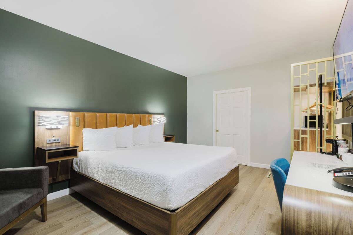 A hotel room with a bed, bedside table, chair, desk, and a door.