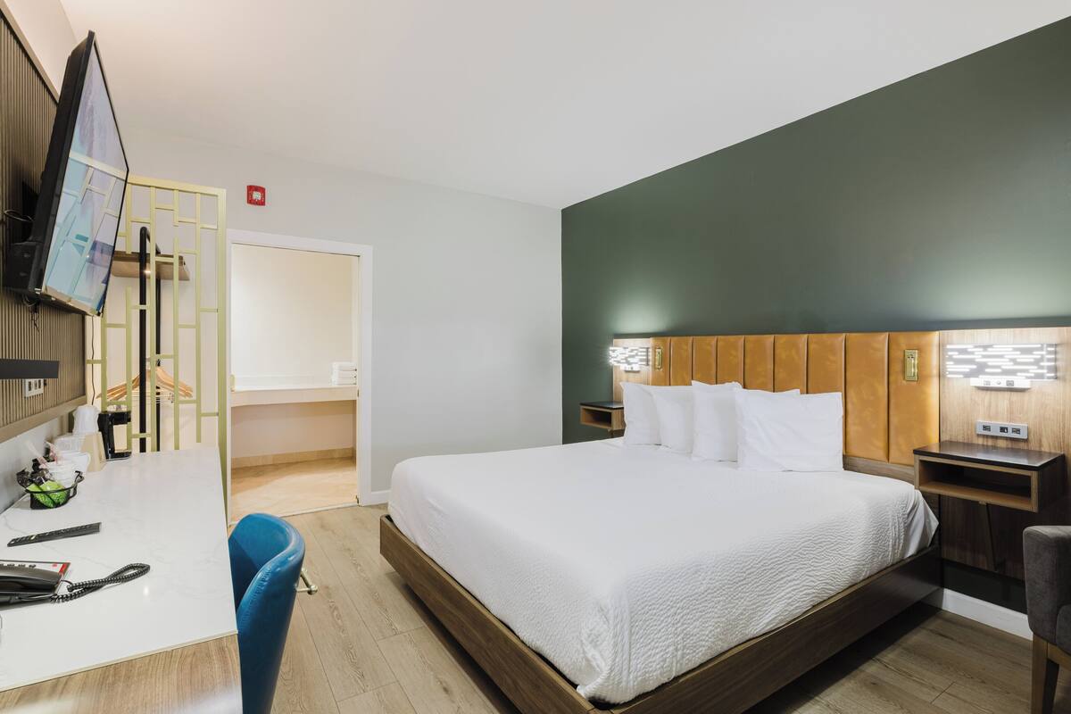 A hotel room with a bed, a desk, a chair, a TV, and a wardrobe.