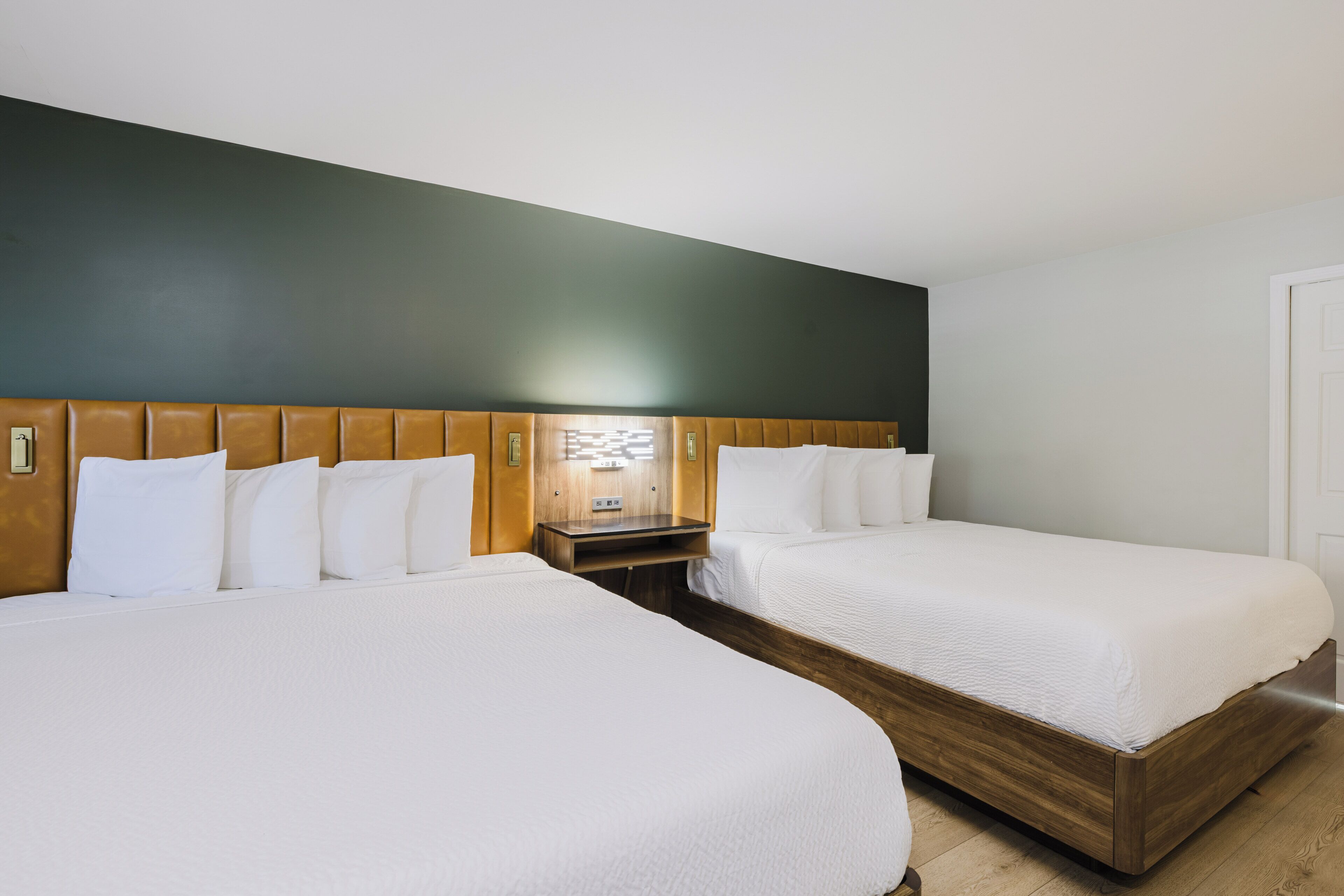A hotel room with two beds, a wooden headboard, a nightstand, and a wall-mounted light fixture.