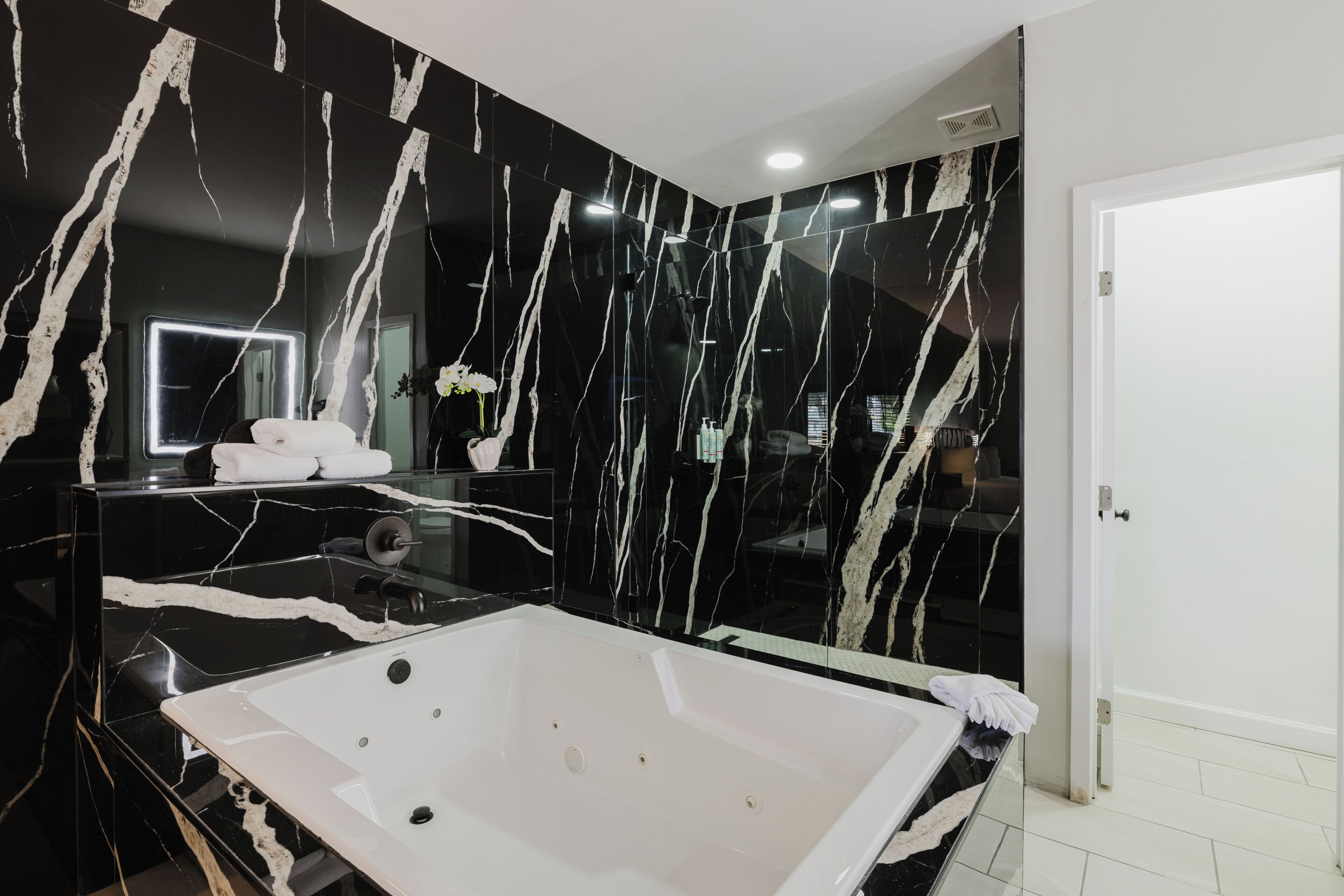 A modern bathroom with a large bathtub, a glass-enclosed shower, and a marble wall with a reflective surface.
