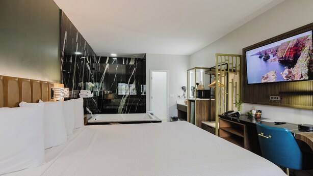Habitación de hotel con una cama grande, un escritorio, televisión y baño con espejo y lavamanos.