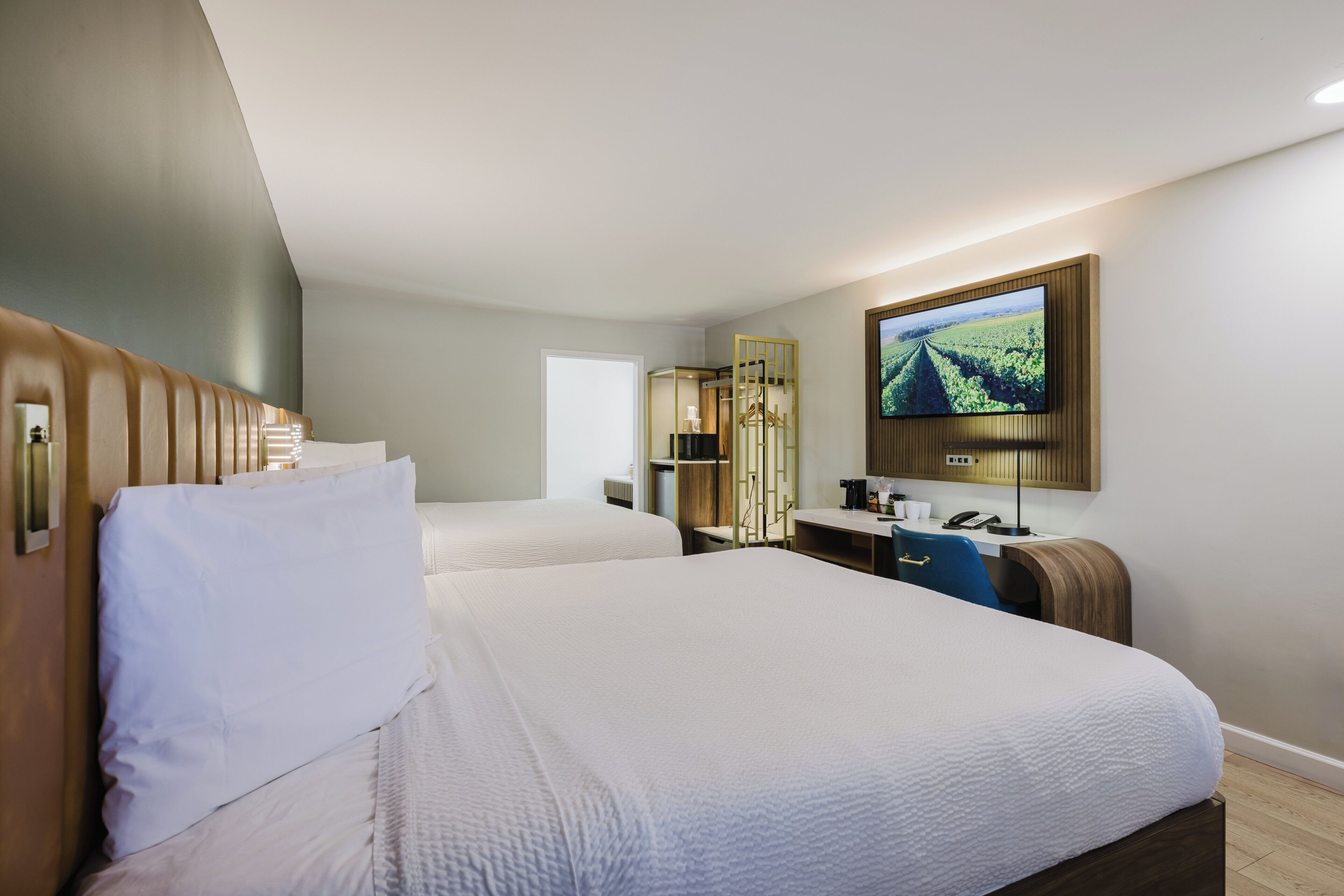 Habitación de hotel con dos camas, un escritorio, televisor y espejo.