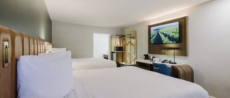 Habitación de hotel con dos camas, un escritorio, televisor y espejo.