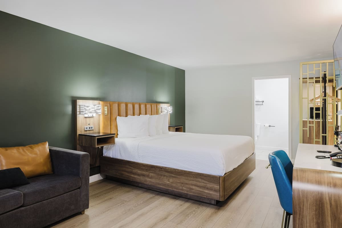 A hotel room with a bed, a desk, a chair, a couch, and a wardrobe.