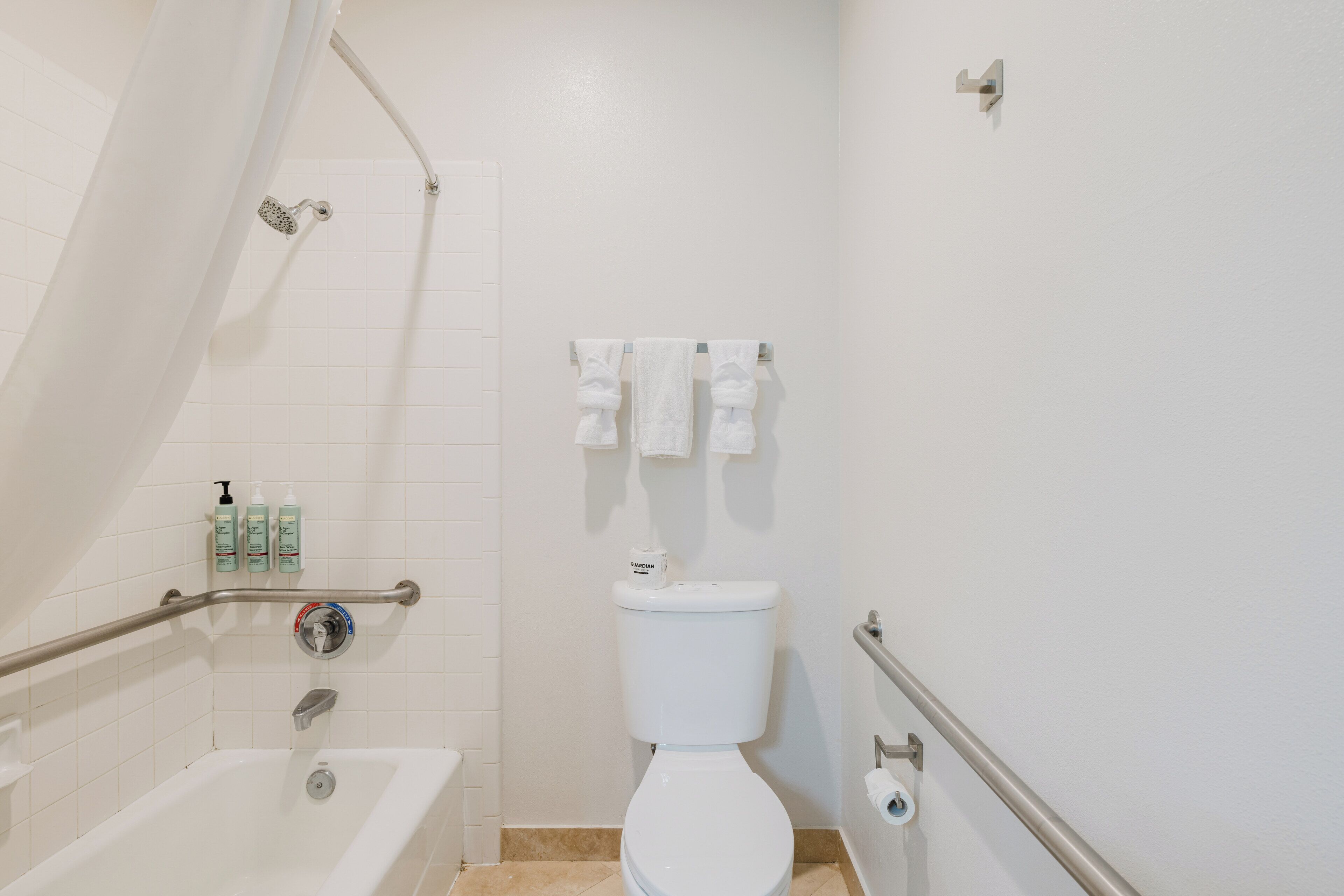 A bathroom with a bathtub, toilet, shower, grab bars, and handrails.