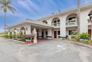 Un hotel de dos pisos, con una estatua frente a él y una alfombra roja que lleva a la entrada.