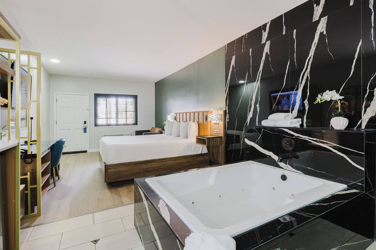 A modern hotel room with a large bed, a separate bathroom with a bathtub, a desk, and a TV.