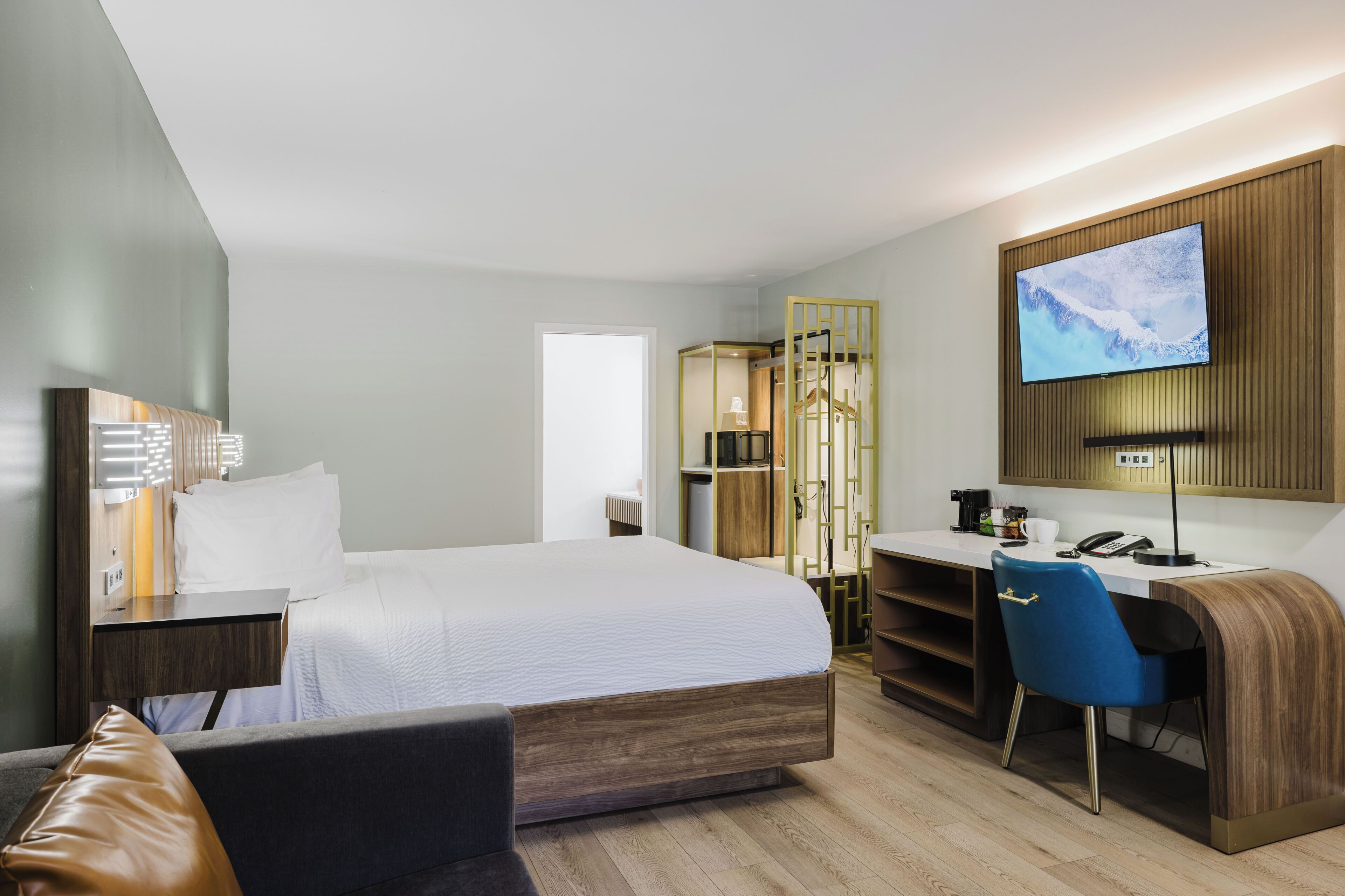 A hotel room with a bed, desk, chair, TV, and a wardrobe.