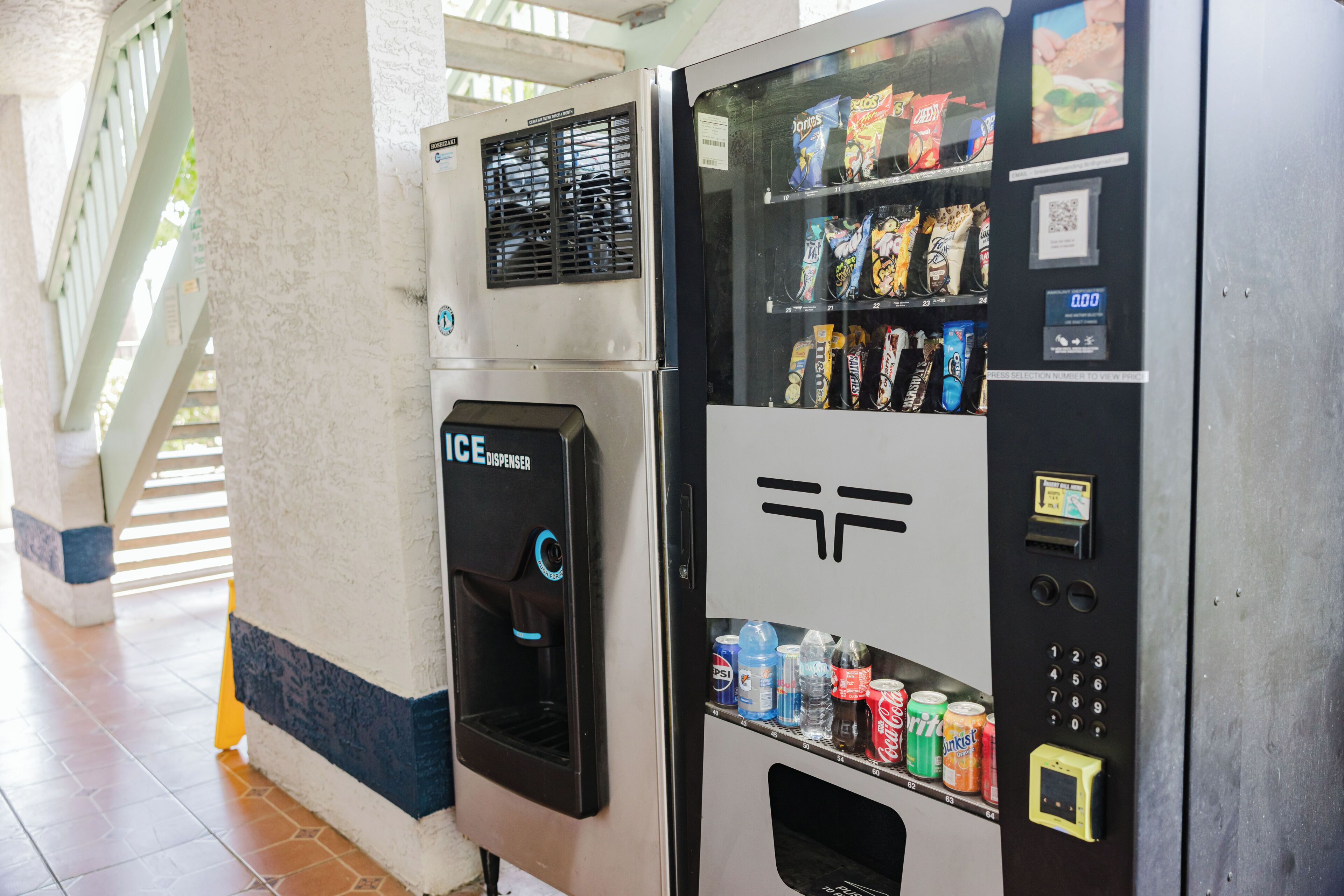 Una máquina expendedora con aperitivos y bebidas, un dispensador de agua y una interfaz de pago digital.