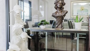 Una mesa de vidrio con un busto, una escultura blanca y dos plantas en macetas.