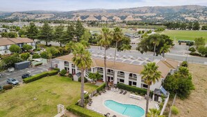 Un edificio de varios pisos con piscina, rodeado de palmeras y vistas a colinas distantes.