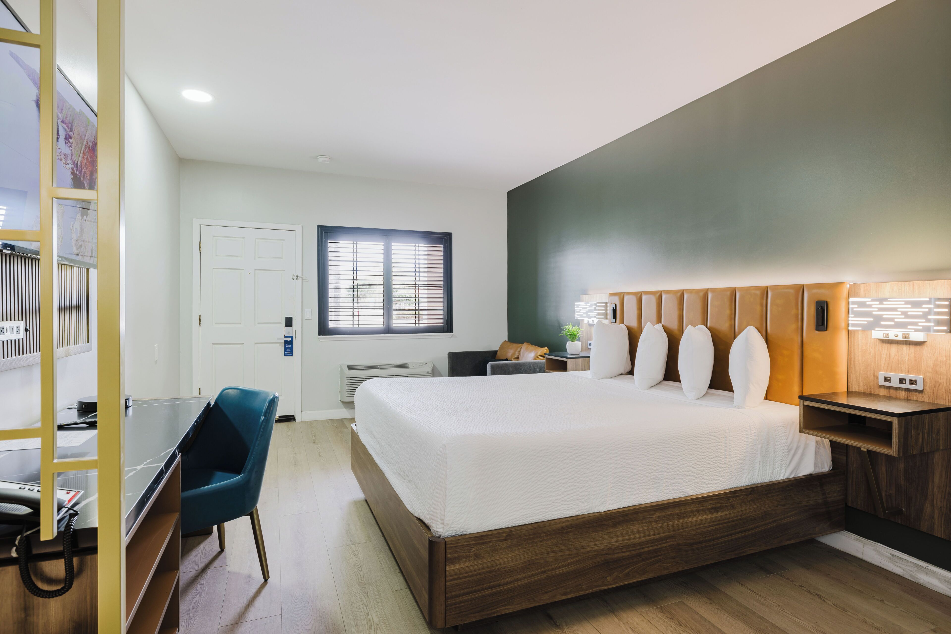 Una habitación de hotel moderna con una cama grande, un escritorio, una silla y una ventana con persianas.