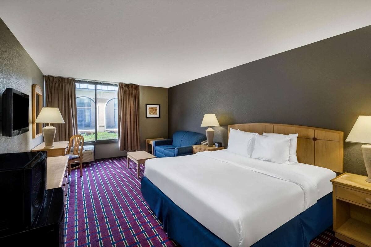 A hotel room with a large bed, a desk with a computer, a chair, a TV, and a window with curtains.