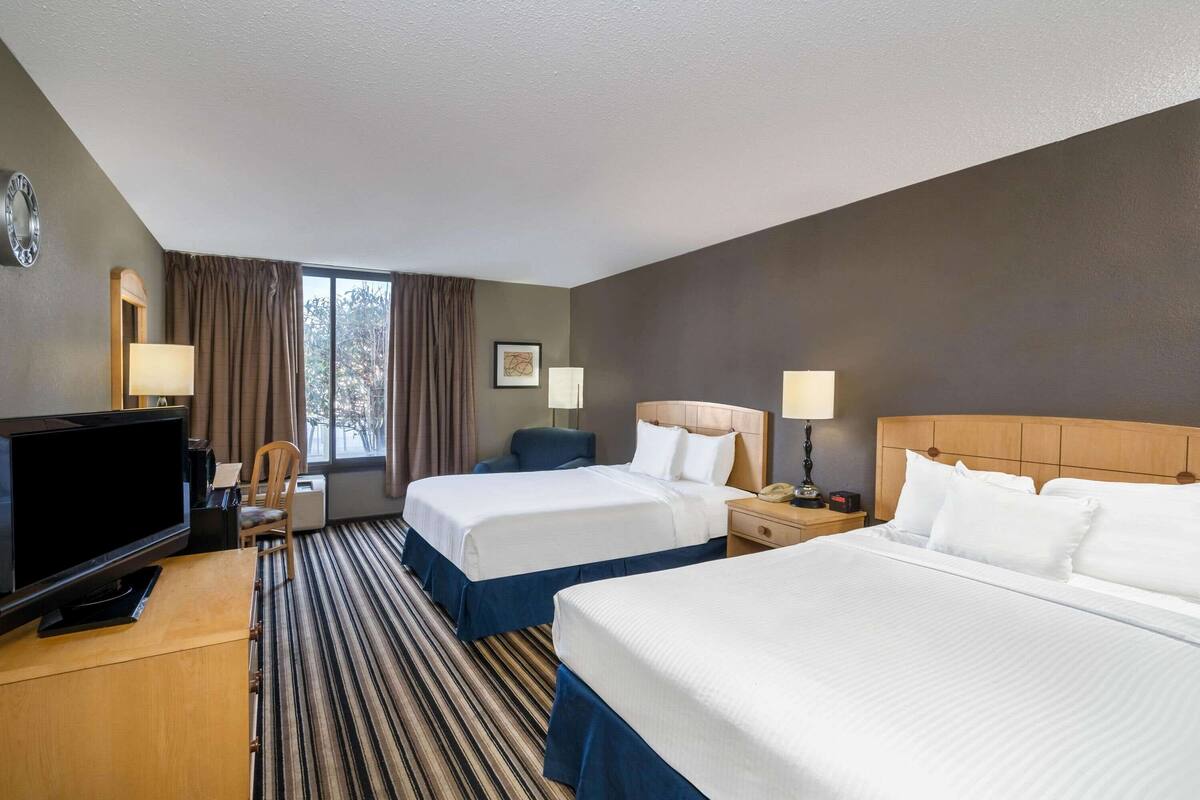 A hotel room with two beds, a TV, a desk, and a window with curtains.