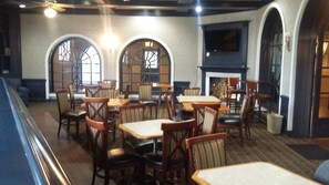 A restaurant interior with wooden tables and chairs, large arched windows, and a fireplace. - Travelodge by Wyndham Memphis Airport/Graceland (Memphis)