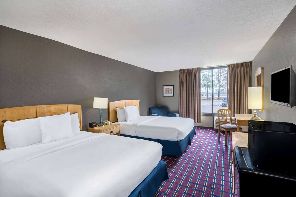 A hotel room with two beds, a desk, a TV, and a window with curtains.