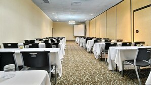 A conference room with rows of tables and chairs, a projector screen, and a patterned carpet. - Travelodge by Wyndham Memphis Airport/Graceland (Memphis)