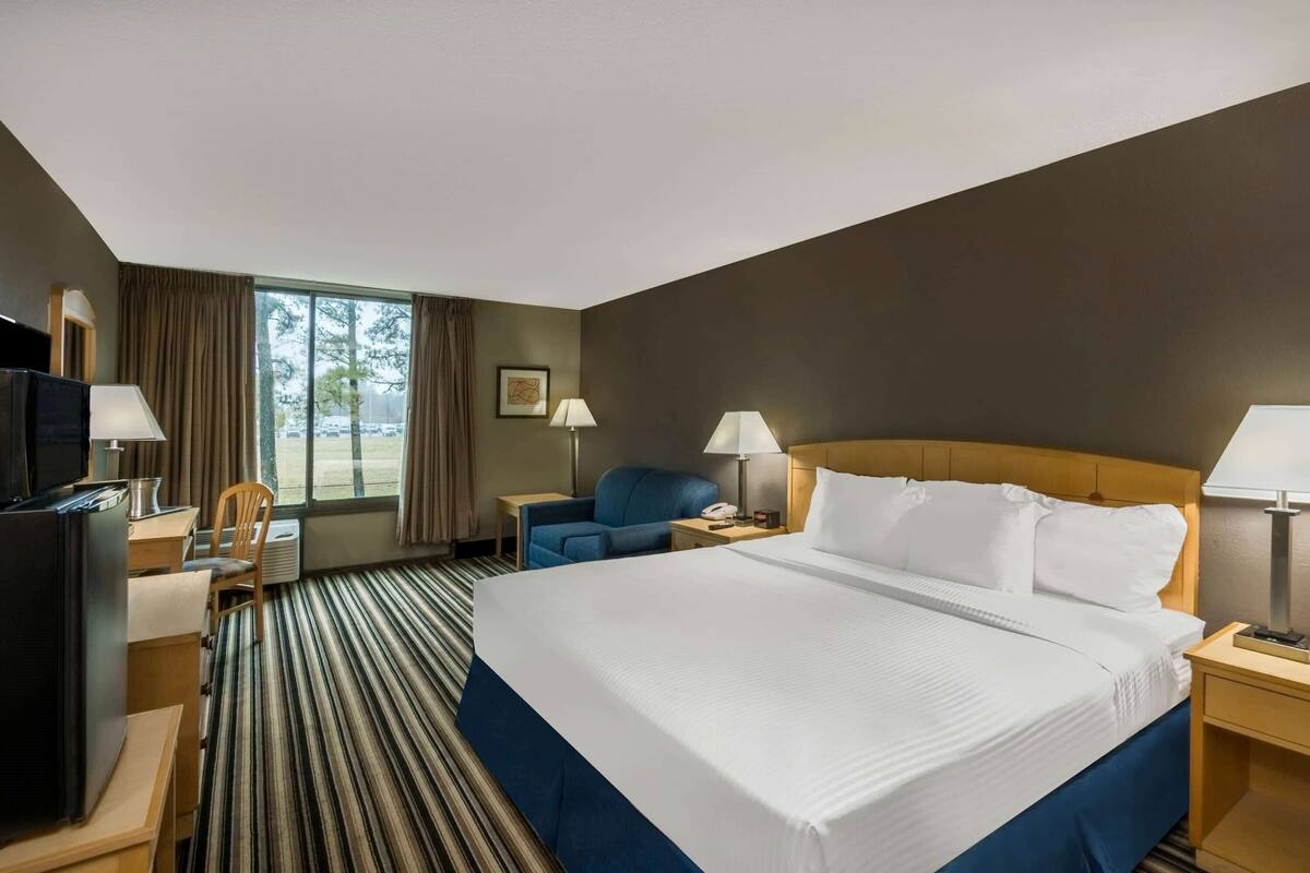 A hotel room with a large bed, a desk, a chair, a TV, and a window with curtains.