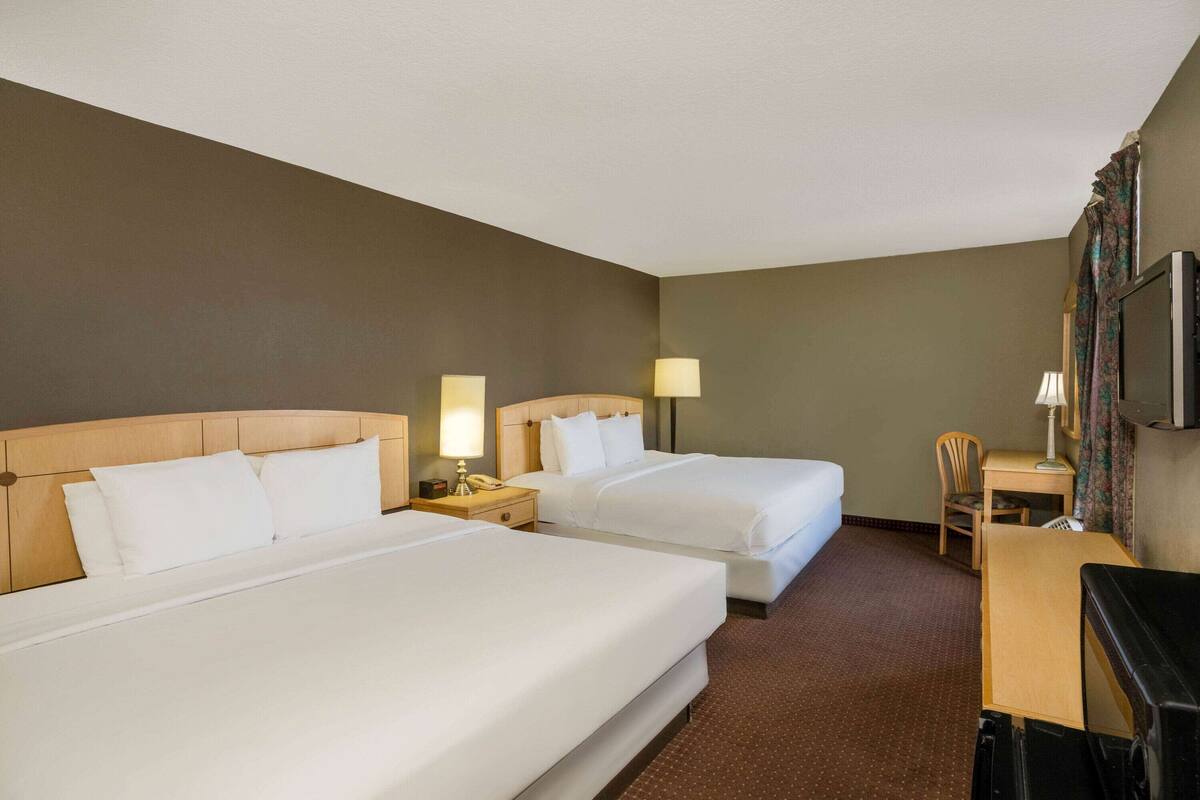 A hotel room with two beds, a desk, a chair, and a TV.