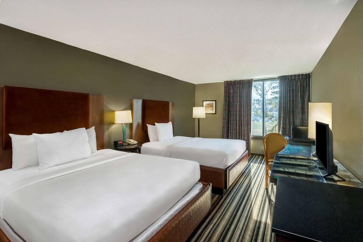 A hotel room with two beds, a desk with a computer, a chair, and a window with curtains.