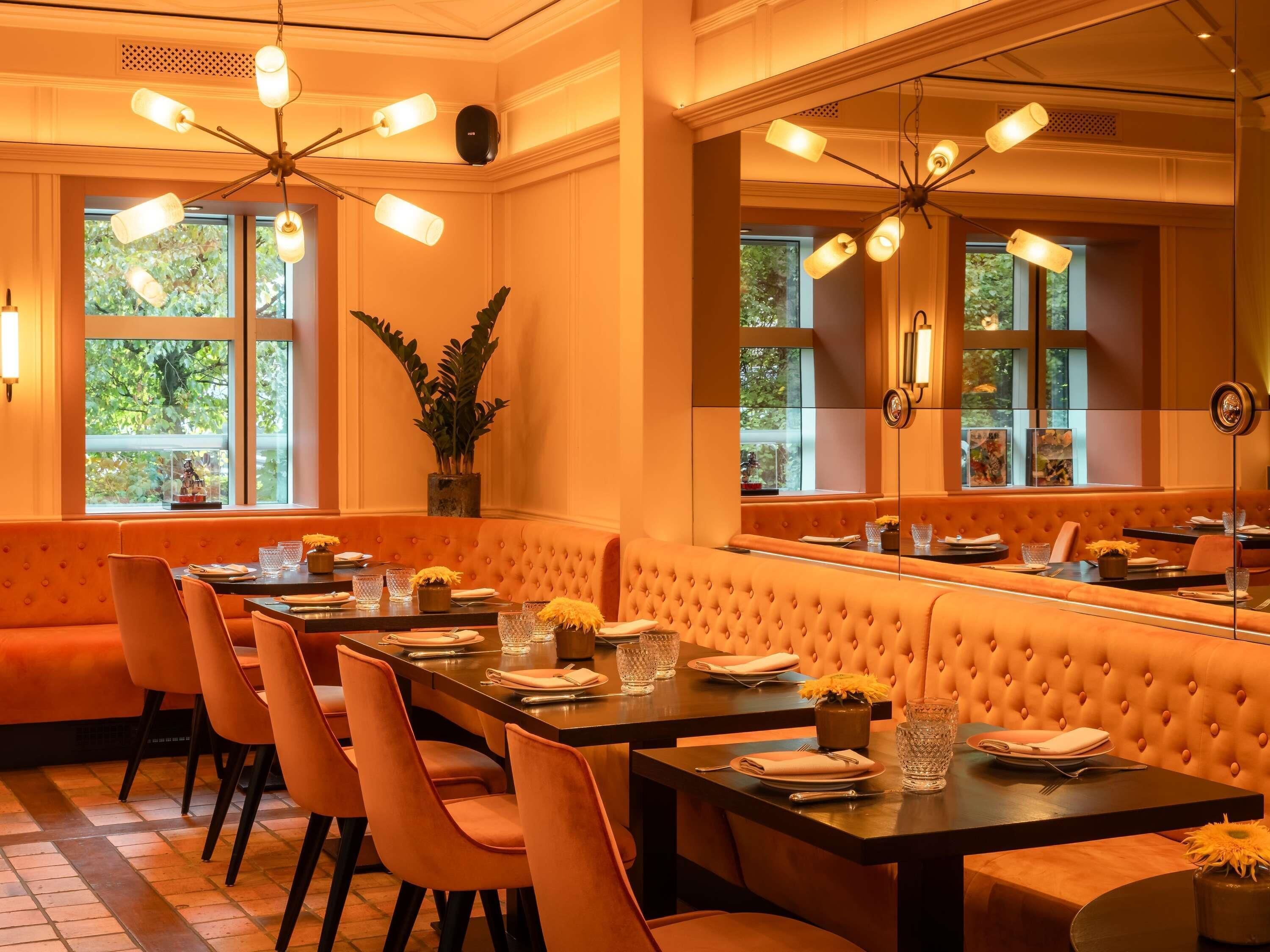 A dining area with a long table, cushioned seating, and pendant lighting.