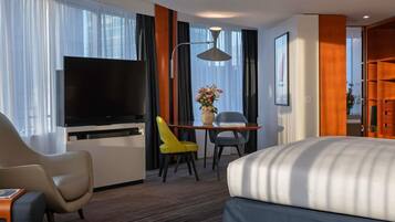 Hotelkamer met een bed, een televisie, een bureau met stoel, een lamp en een raam met gordijnen.