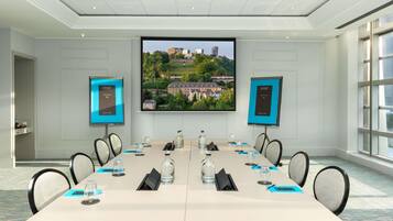 Une salle de conférence équipée d’une grande table, de chaises, d’un écran de projection et de deux écrans d’accueil.