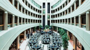 A multi-level atrium with a central open space surrounded by tables and chairs, large columns, and a glass ceiling.