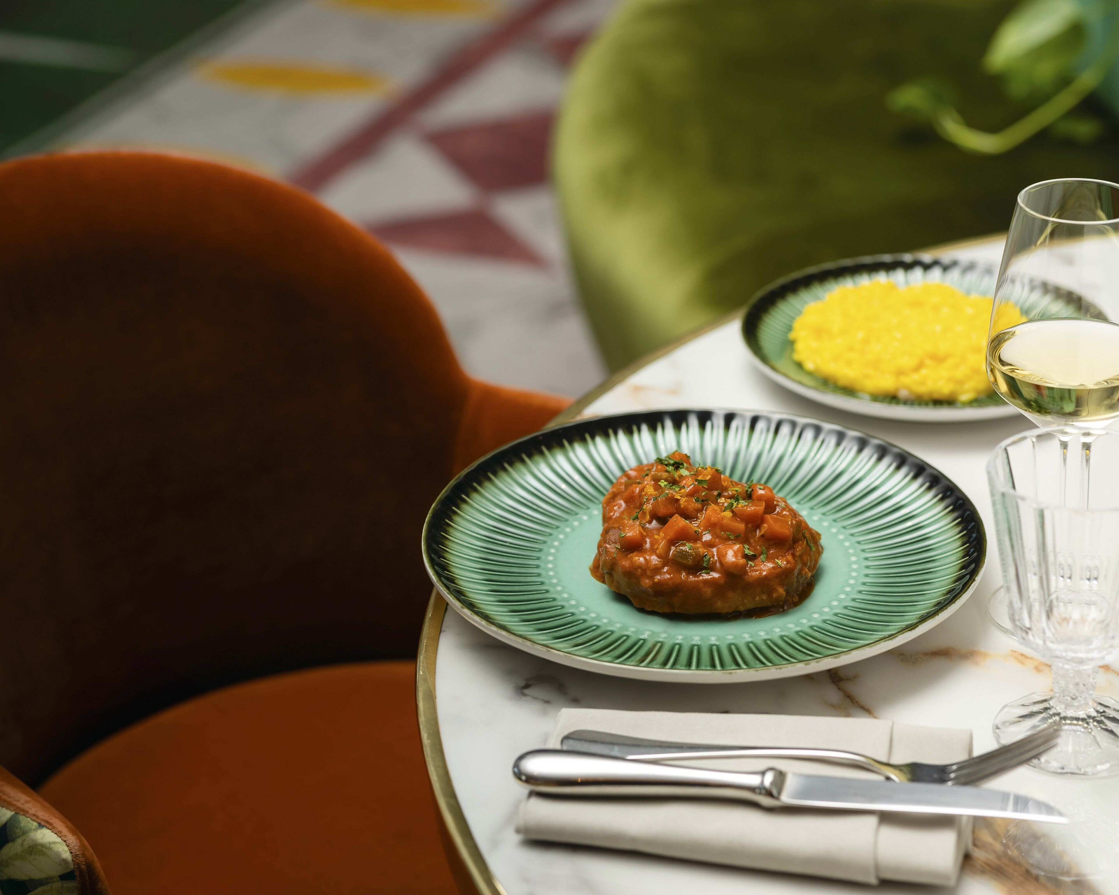 A table with a plate of food, a glass of white wine, and a napkin with a fork.