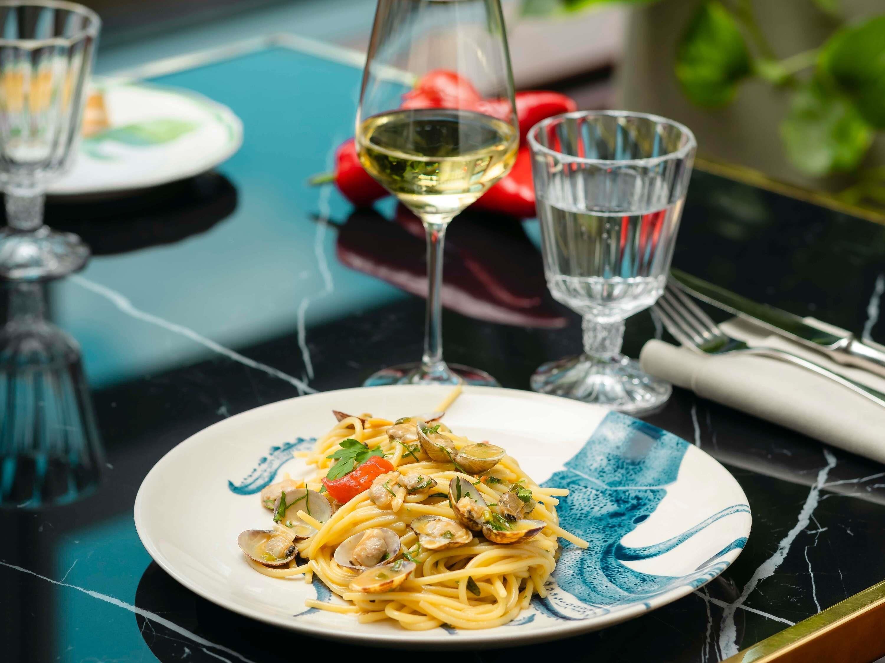 A plate of pasta with clams and a glass of white wine on a table.