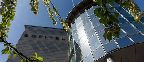 Un edificio moderno con el nombre 'SOFITEL' en su fachada, rodeado de árboles en flor.