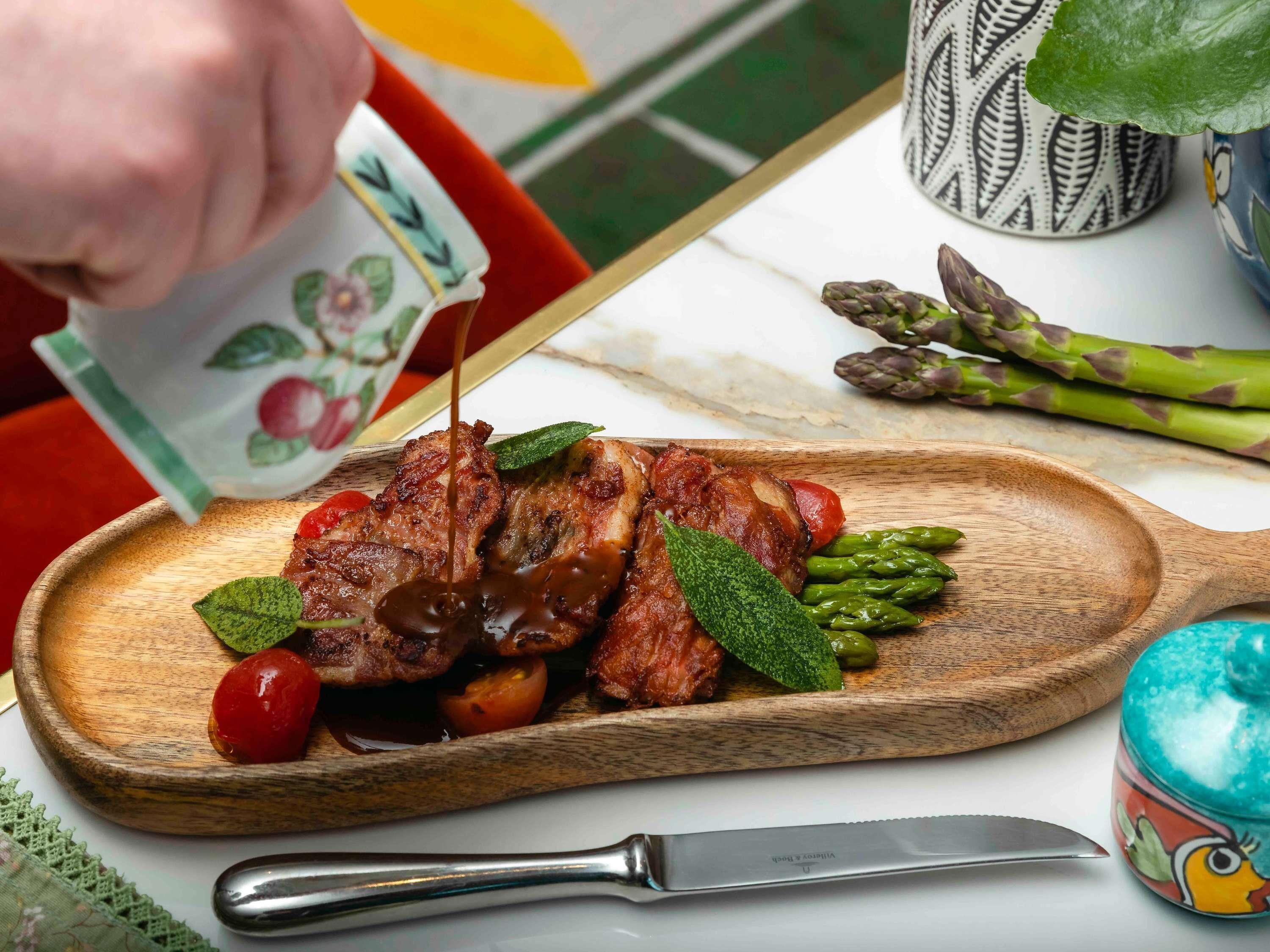 A wooden serving board with grilled meat, cherry tomatoes, and asparagus.