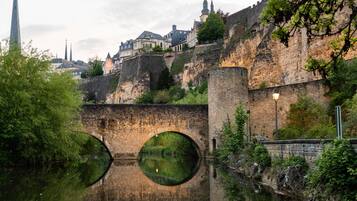 A historic stone bridge with circular openings over a river, leading to a fortified city with medieval architecture.