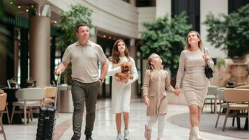 A family walking through a hotel lobby with a dining area and plants in the background.
