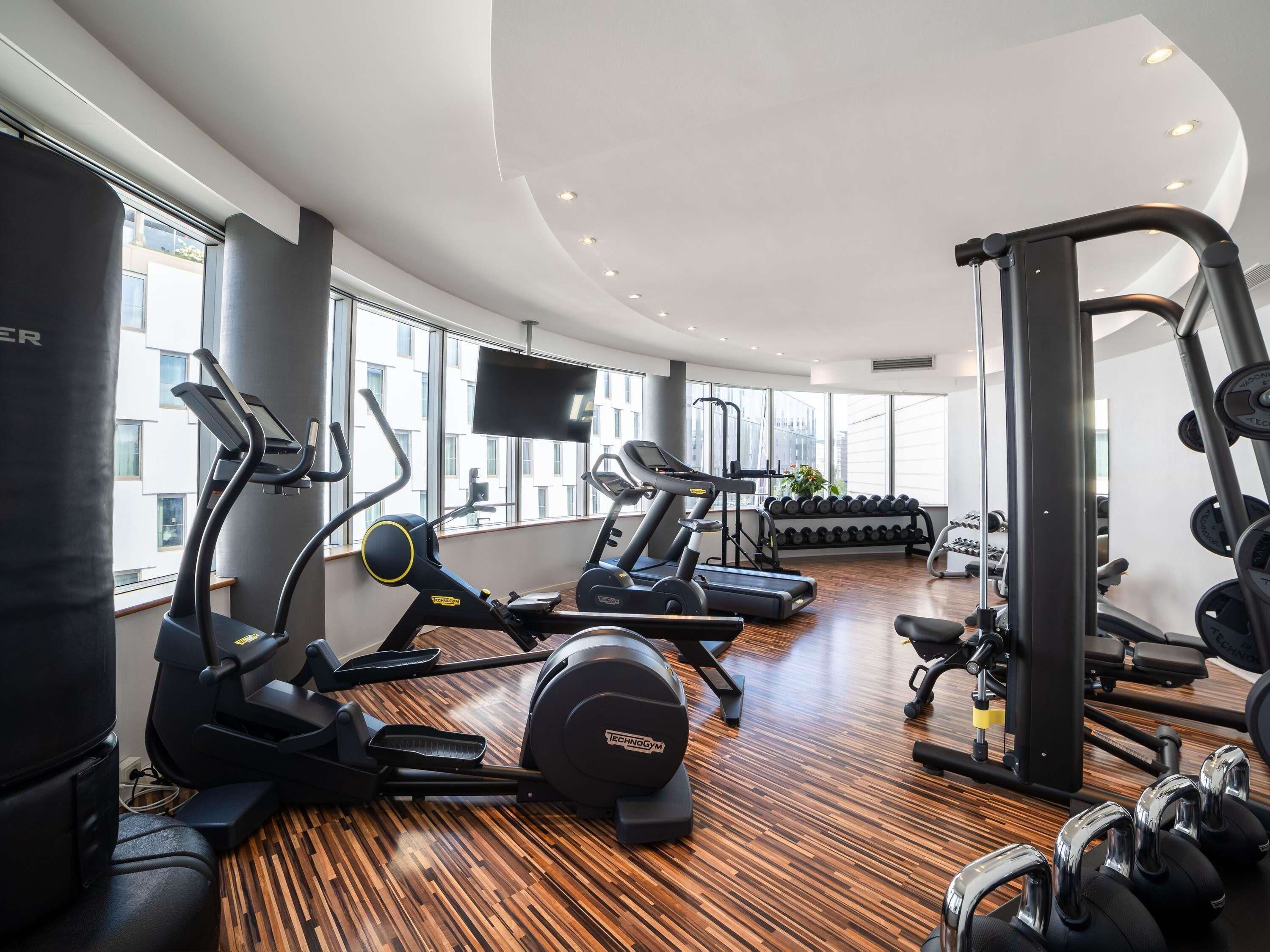 Un gimnasio moderno con máquinas de cardio, pesas libres y una pantalla de televisión.