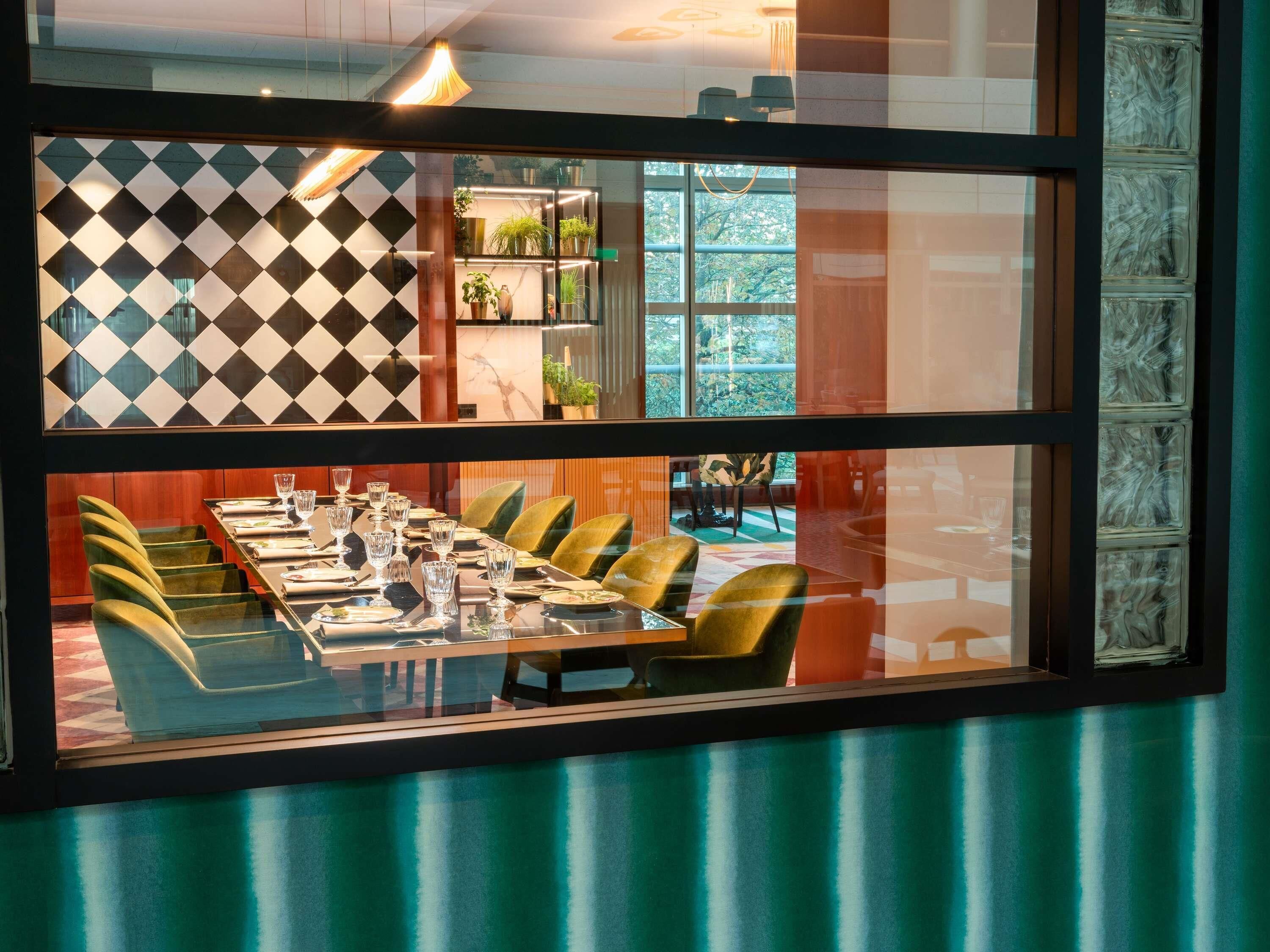 A dining area with a checkered wall, a long table set with plates and glasses, and green chairs.