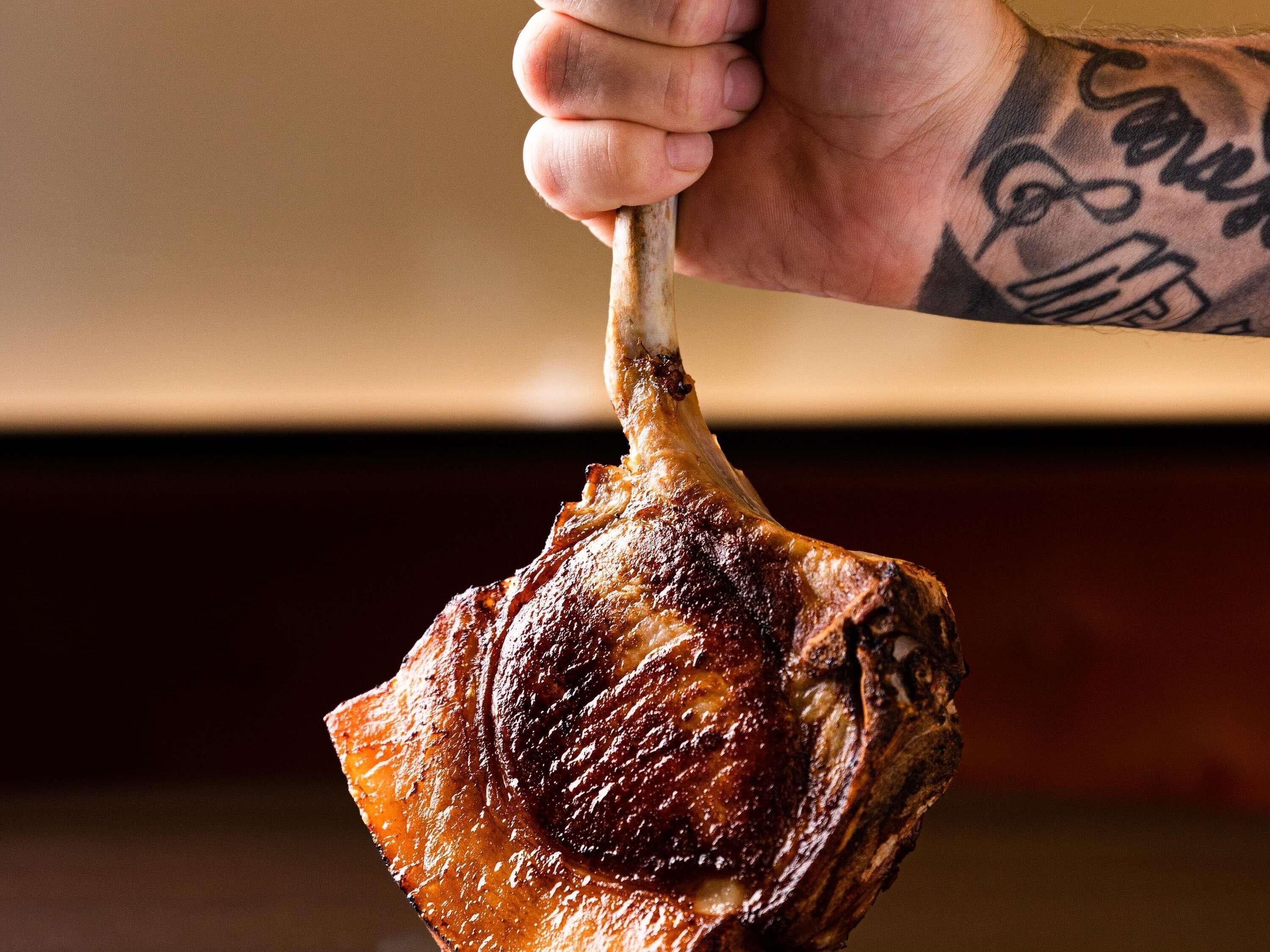 A hand holding a cooked piece of meat, likely a roast, with a visible bone.