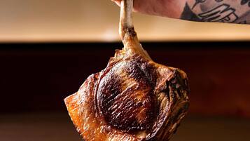 A hand holding a cooked piece of meat, likely a roast, with a visible bone.
